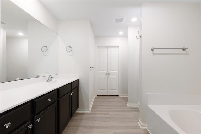 full bathroom with a tub to relax in, wood finished floors, vanity, visible vents, and baseboards