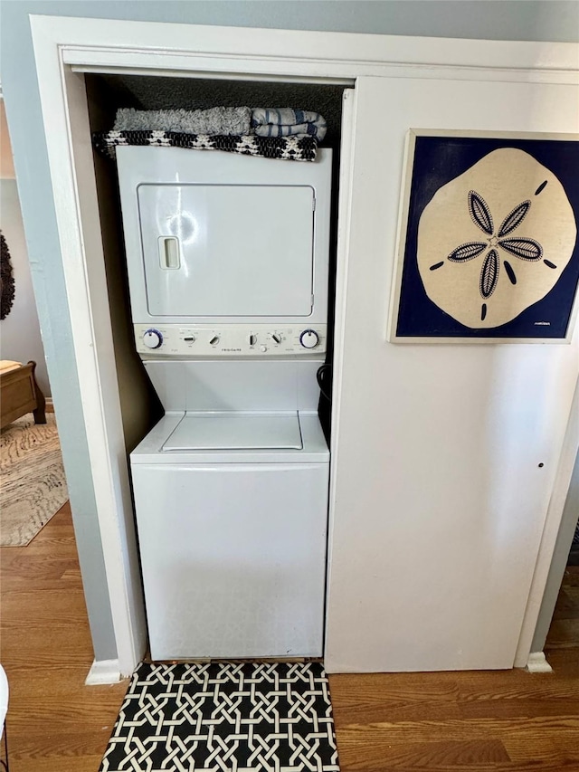 laundry area featuring laundry area, wood finished floors, and stacked washer and clothes dryer