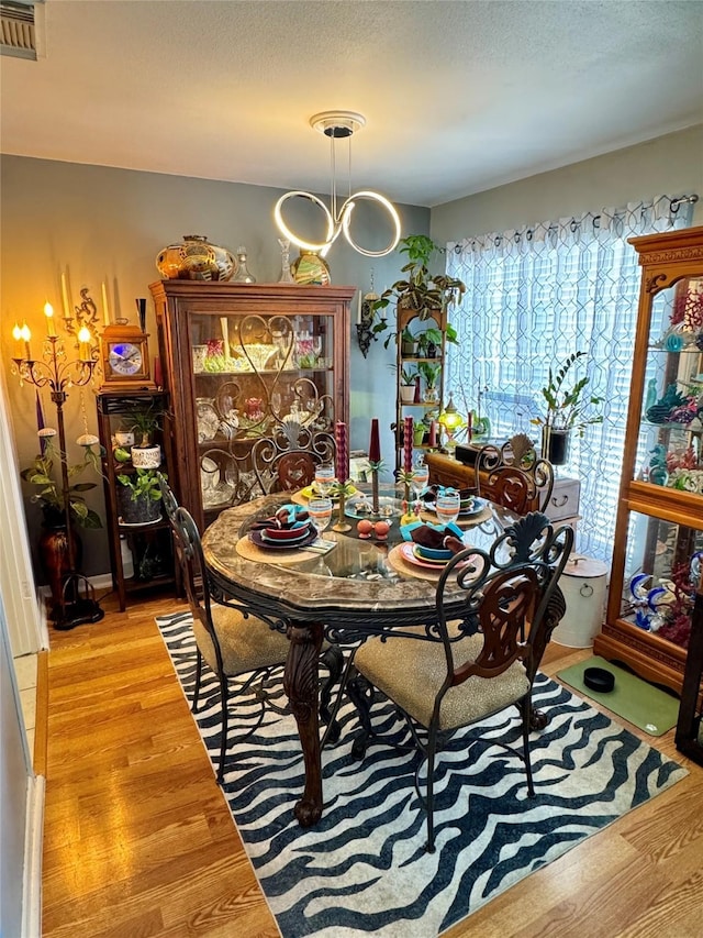 dining room featuring a textured ceiling, light wood finished floors, a chandelier, and visible vents