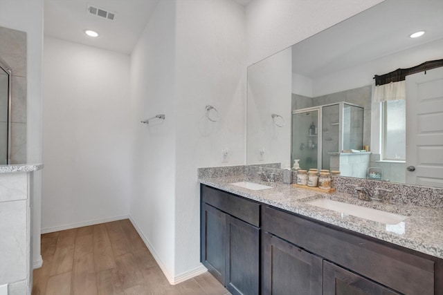 full bath featuring visible vents, a sink, a shower stall, and wood finished floors