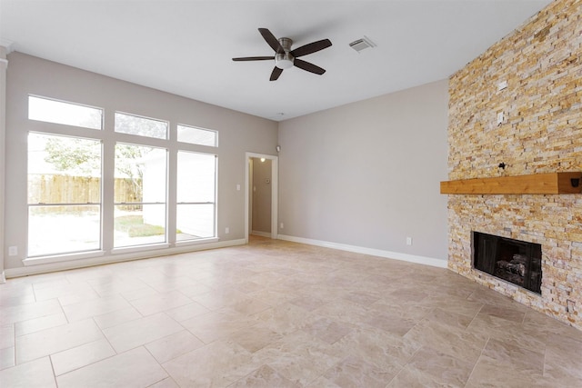 unfurnished living room featuring baseboards, visible vents, a ceiling fan, and a stone fireplace