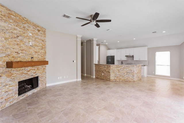 unfurnished living room featuring ornate columns, visible vents, ceiling fan, a stone fireplace, and baseboards