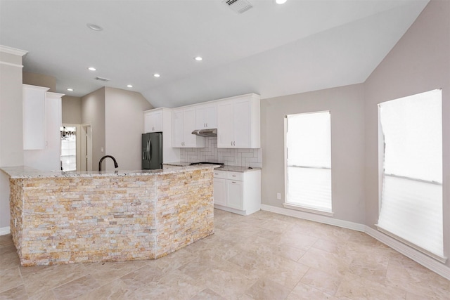 kitchen featuring lofted ceiling, under cabinet range hood, black fridge with ice dispenser, visible vents, and light stone countertops