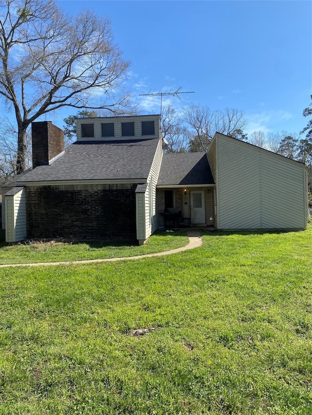 view of front of home featuring a front yard, roof with shingles, a chimney, and an outbuilding