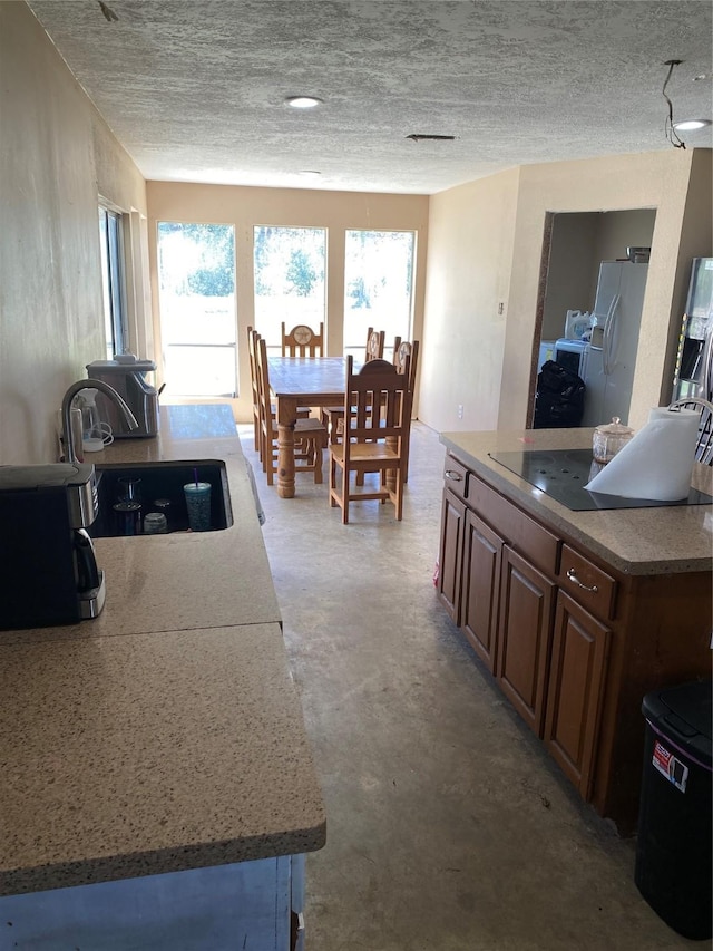 kitchen featuring concrete flooring, a textured ceiling, black electric stovetop, a sink, and white fridge with ice dispenser