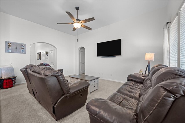 living area with arched walkways, ceiling fan, baseboards, and light colored carpet