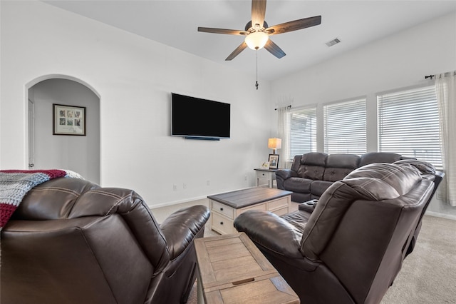 living room featuring arched walkways, light colored carpet, visible vents, a ceiling fan, and baseboards