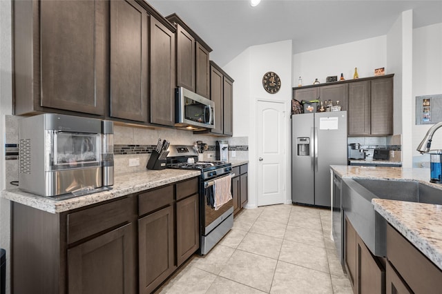 kitchen with light stone counters, appliances with stainless steel finishes, backsplash, and dark brown cabinets