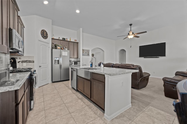 kitchen with arched walkways, appliances with stainless steel finishes, open floor plan, dark brown cabinetry, and a sink