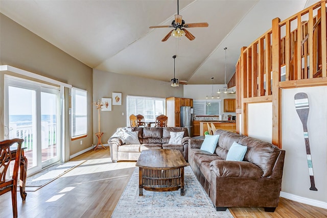 living area featuring high vaulted ceiling, baseboards, ceiling fan, and light wood finished floors