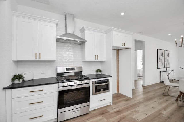 kitchen with wall chimney range hood, dark countertops, appliances with stainless steel finishes, and white cabinets