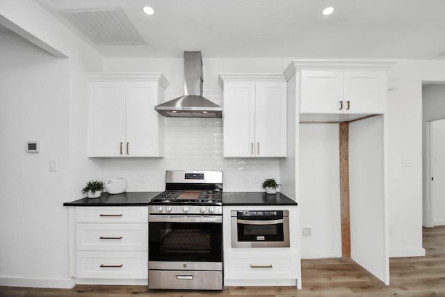 kitchen with dark countertops, visible vents, backsplash, appliances with stainless steel finishes, and wall chimney range hood