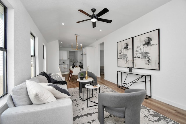 living area with baseboards, ceiling fan with notable chandelier, light wood-style flooring, and recessed lighting