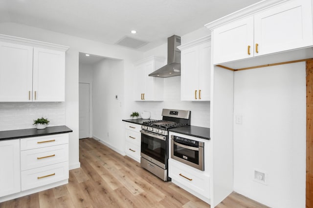 kitchen featuring light wood finished floors, wall chimney exhaust hood, appliances with stainless steel finishes, and dark countertops