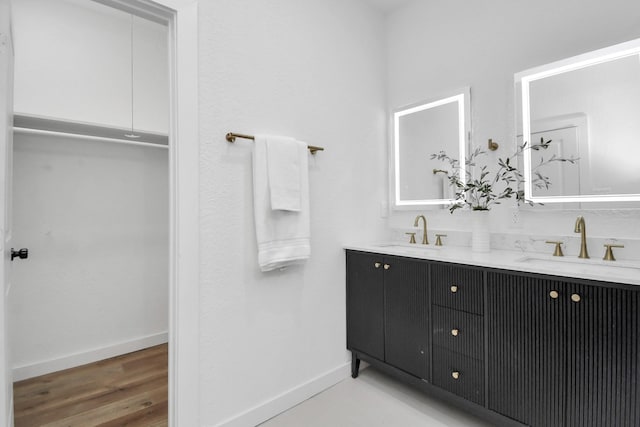 bathroom with wood finished floors, a sink, baseboards, and double vanity