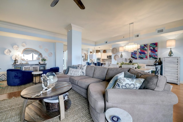 living room featuring visible vents, ceiling fan with notable chandelier, wood finished floors, and ornamental molding