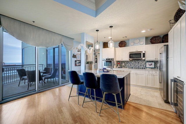 kitchen with backsplash, beverage cooler, light wood-type flooring, white cabinets, and stainless steel appliances