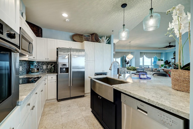 kitchen featuring a sink, light stone counters, white cabinetry, stainless steel appliances, and hanging light fixtures