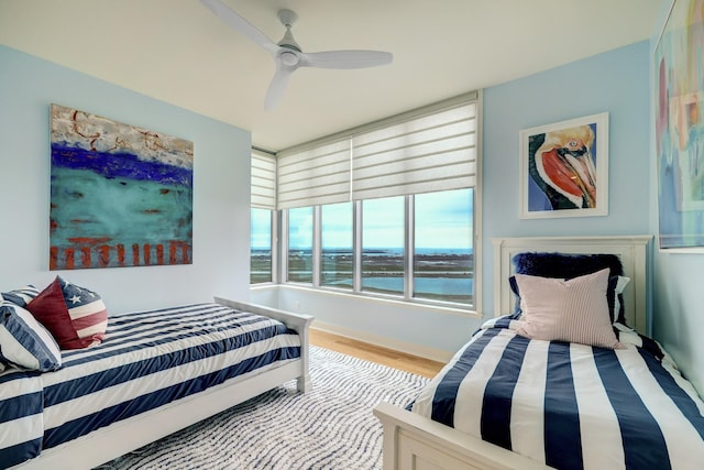 bedroom featuring a water view, wood finished floors, and a ceiling fan