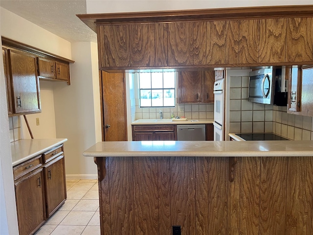 kitchen with backsplash, stainless steel appliances, a peninsula, light countertops, and light tile patterned floors