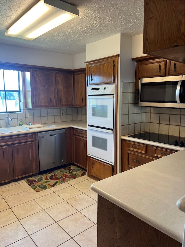 kitchen with a sink, backsplash, a textured ceiling, appliances with stainless steel finishes, and light countertops