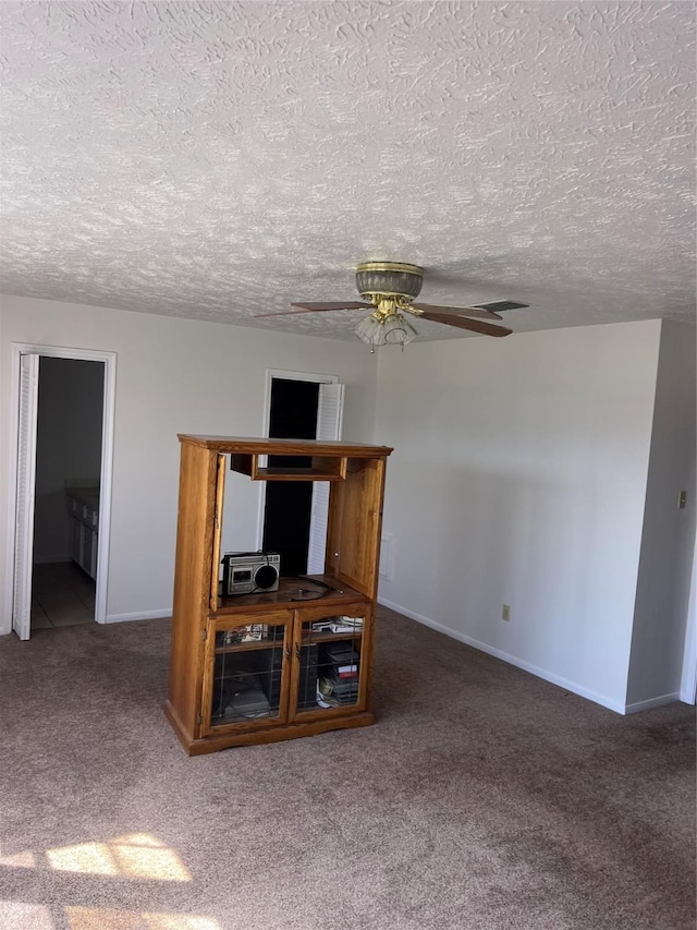 unfurnished living room featuring carpet, visible vents, baseboards, ceiling fan, and a textured ceiling