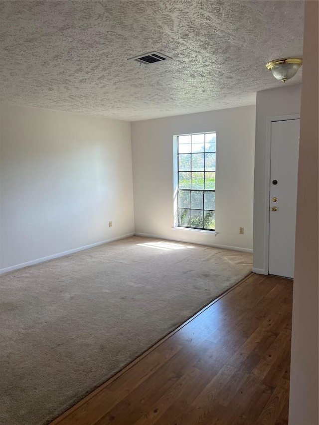 empty room featuring wood finished floors, baseboards, visible vents, carpet floors, and a textured ceiling