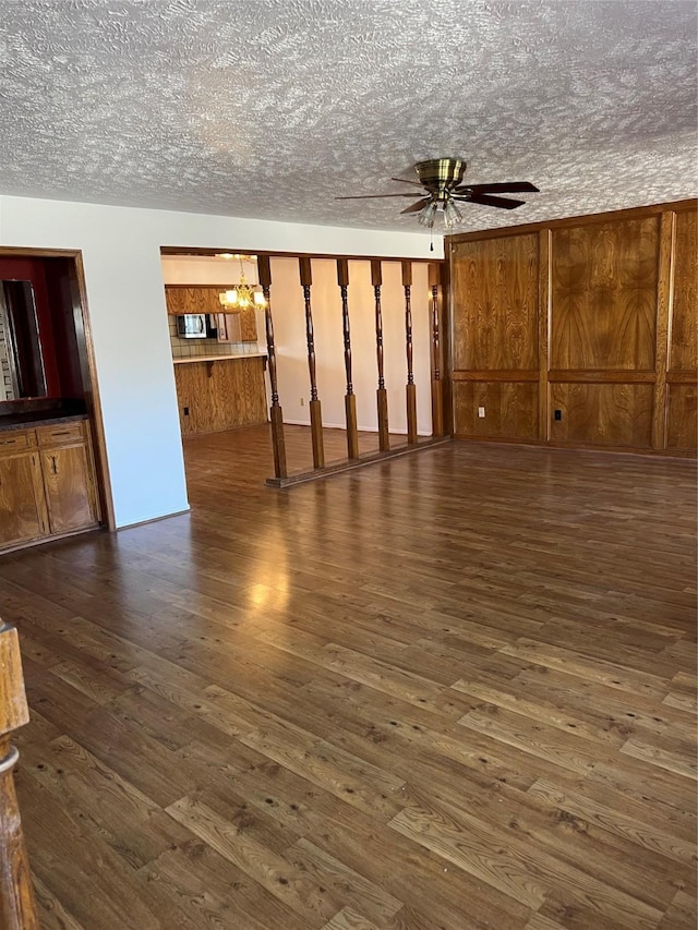 unfurnished living room with dark wood-type flooring, ceiling fan with notable chandelier, and a textured ceiling