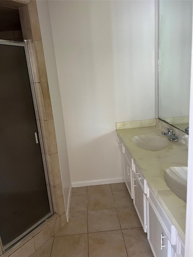 full bath with baseboards, double vanity, a stall shower, a sink, and tile patterned floors