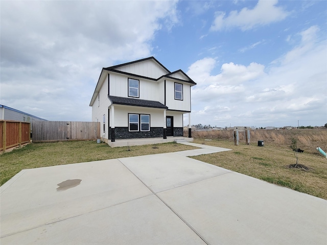 view of front facade featuring stone siding, a patio, a fenced backyard, board and batten siding, and a front yard