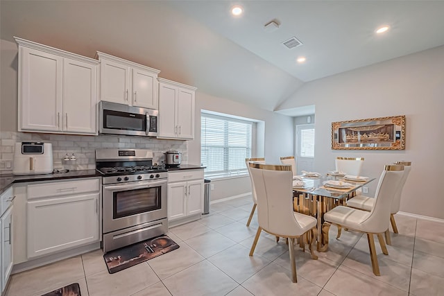 kitchen featuring lofted ceiling, light tile patterned flooring, stainless steel appliances, dark countertops, and backsplash