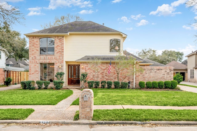 view of front of house with a front yard, french doors, brick siding, and roof with shingles