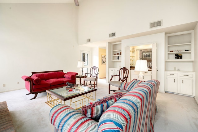 living area featuring a high ceiling, built in shelves, visible vents, and light carpet