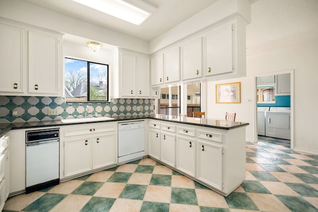 kitchen with dark countertops, a peninsula, decorative backsplash, dishwasher, and washing machine and clothes dryer