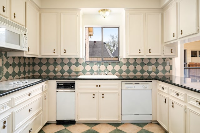 kitchen featuring decorative backsplash, white appliances, dark countertops, and a sink