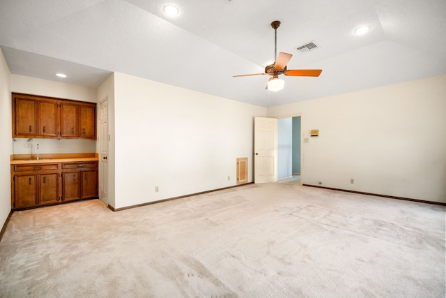 empty room featuring vaulted ceiling, light colored carpet, baseboards, and ceiling fan