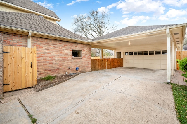 view of property exterior featuring fence, concrete driveway, a shingled roof, a garage, and brick siding