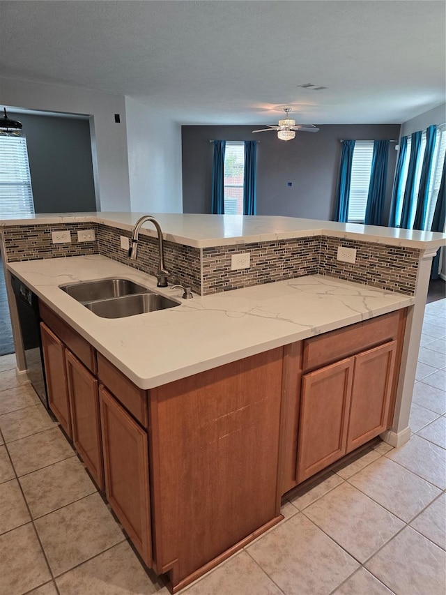 kitchen with dishwasher, backsplash, a sink, and a kitchen island with sink