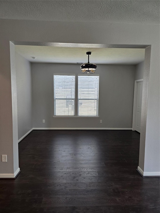 unfurnished dining area with a textured ceiling, dark wood-style flooring, and baseboards