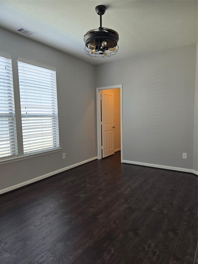 empty room featuring dark wood-style floors, a wealth of natural light, visible vents, and baseboards