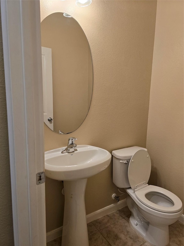 half bathroom with baseboards, toilet, and tile patterned floors