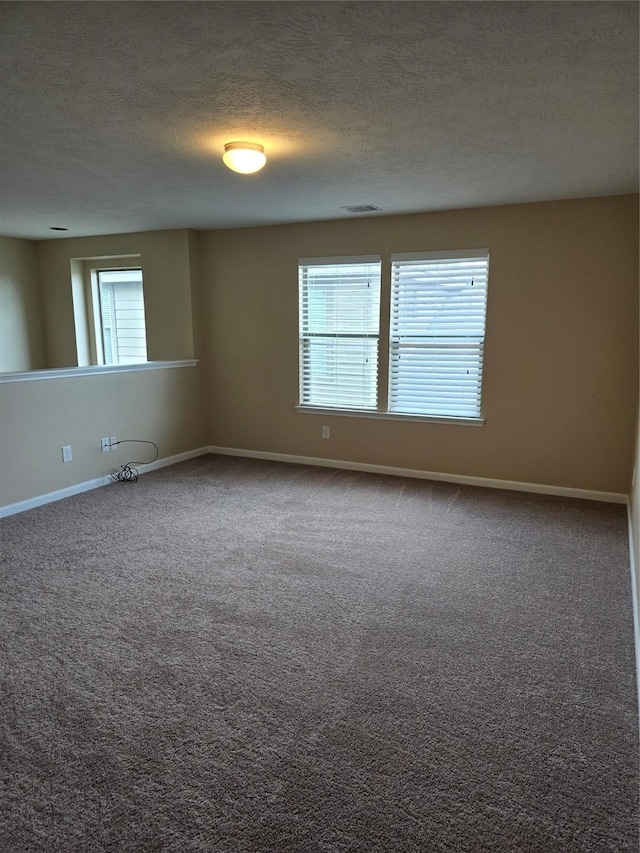 carpeted spare room featuring a textured ceiling, visible vents, and baseboards