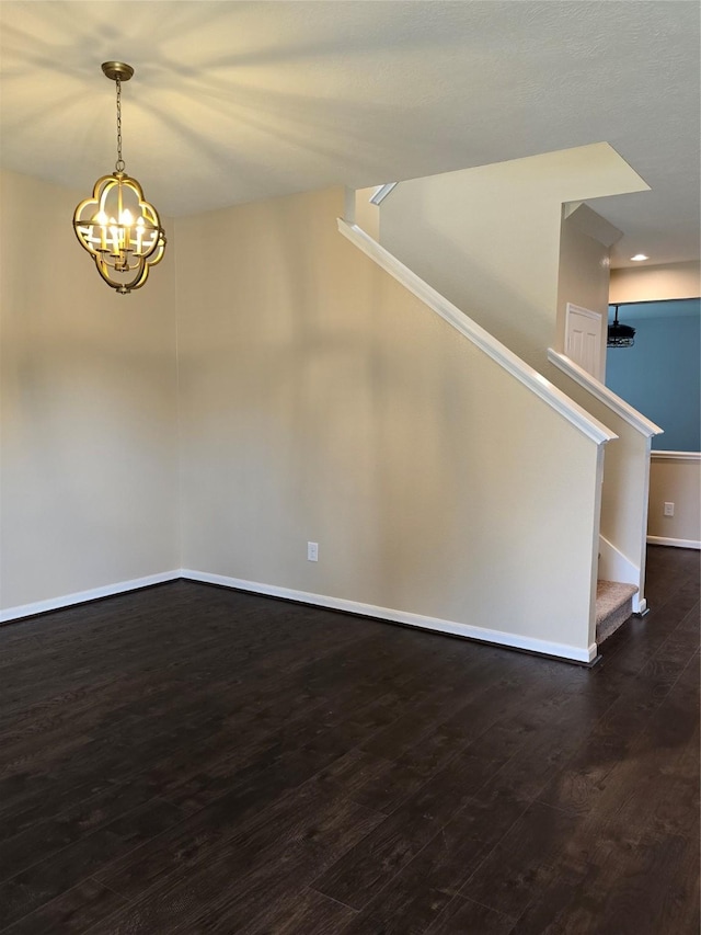 unfurnished room featuring dark wood finished floors, stairway, baseboards, and an inviting chandelier