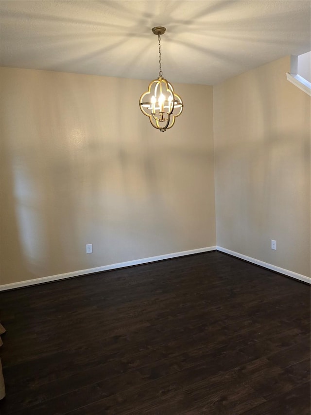 spare room with a chandelier, dark wood-style flooring, and baseboards