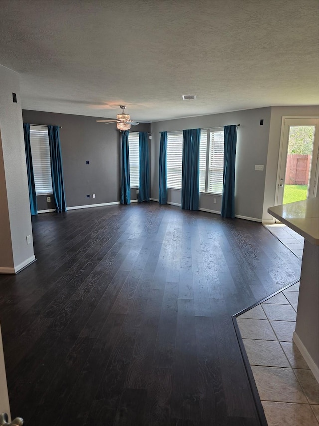 empty room featuring baseboards, dark wood finished floors, a textured ceiling, visible vents, and a ceiling fan
