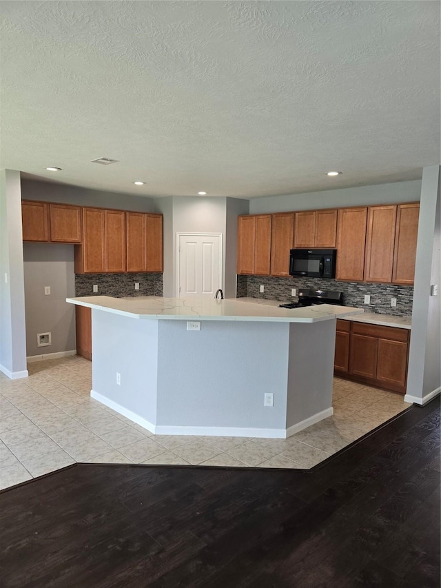 kitchen featuring light countertops, brown cabinetry, light wood-type flooring, black microwave, and a large island with sink