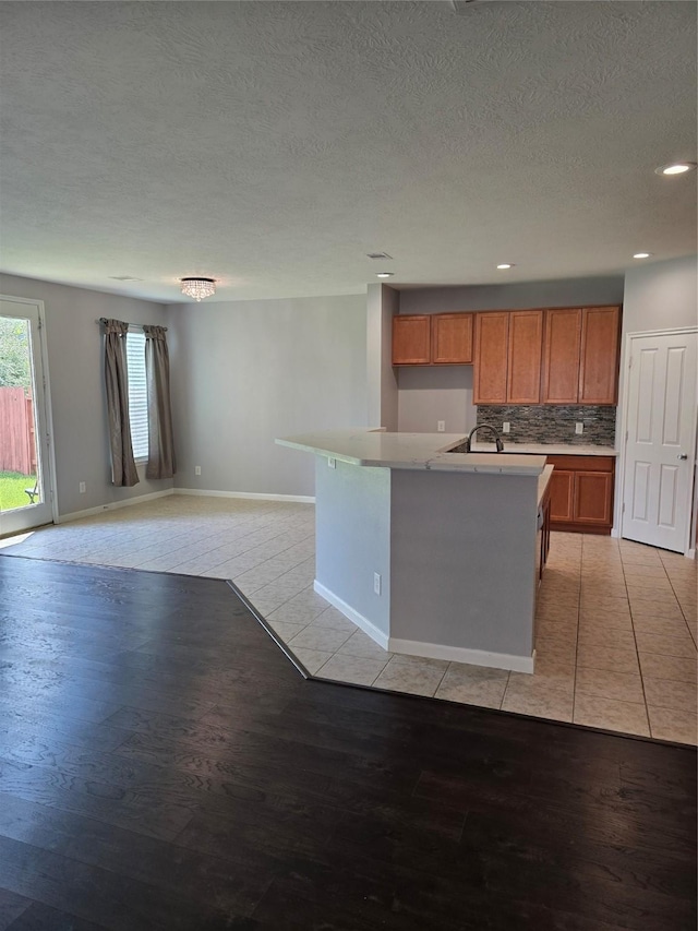 kitchen featuring tasteful backsplash, brown cabinets, a kitchen island with sink, light countertops, and light wood-type flooring