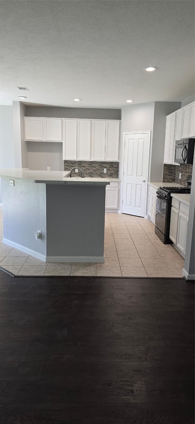 kitchen with a sink, white cabinetry, black appliances, light wood-style floors, and decorative backsplash