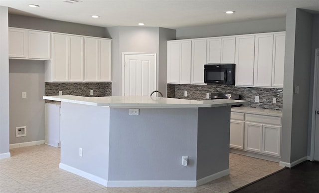 kitchen with a kitchen island with sink, black microwave, light countertops, and white cabinets