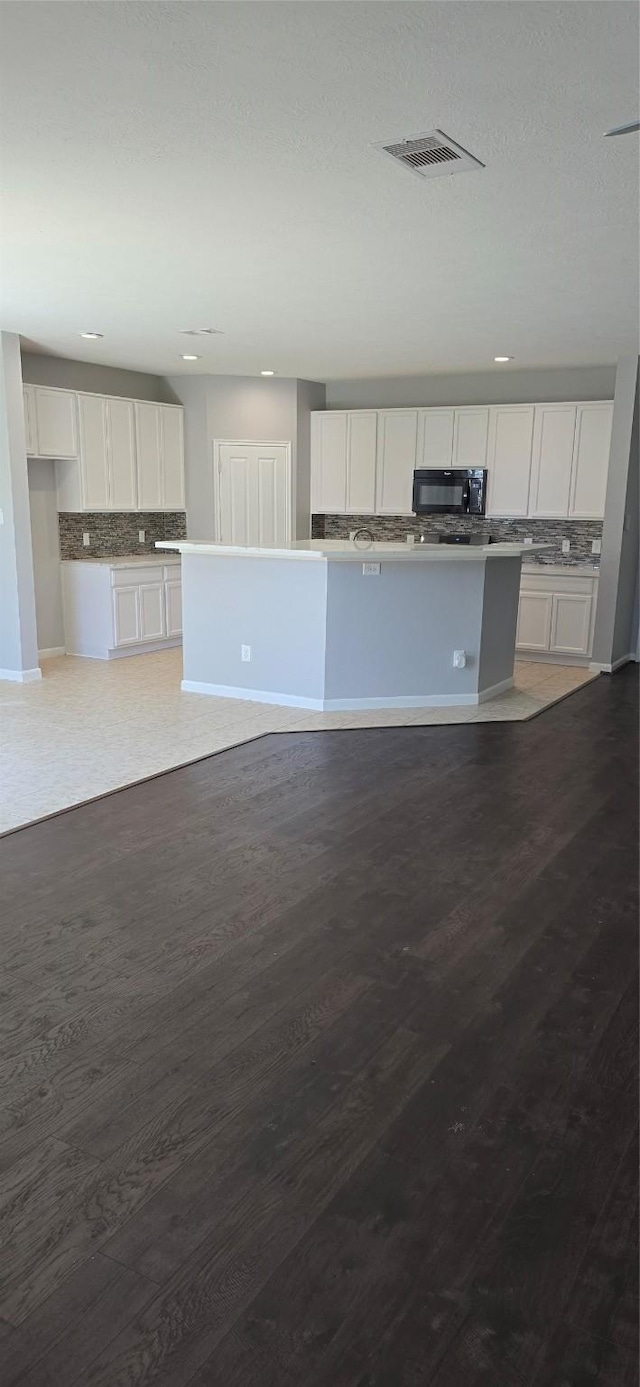 kitchen with white cabinetry, decorative backsplash, black microwave, and visible vents
